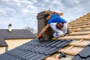 Close view of a roofer fitting metal flashing around a roof vent on a shingled roof.
